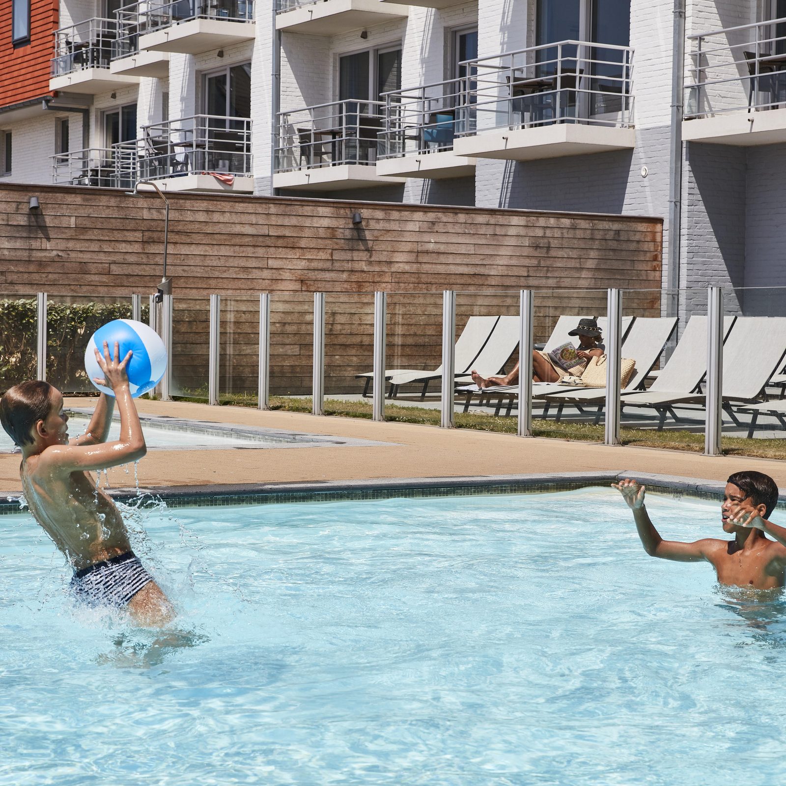 Twee jongens die met een strandbal spelen in het buitenzwembad bij Holiday Suites Zeebrugge