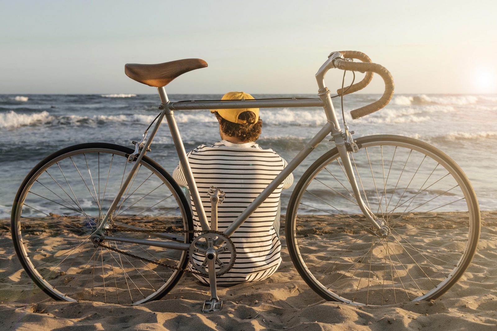 Man zittend op strand met racefiets uitkijkend over zee