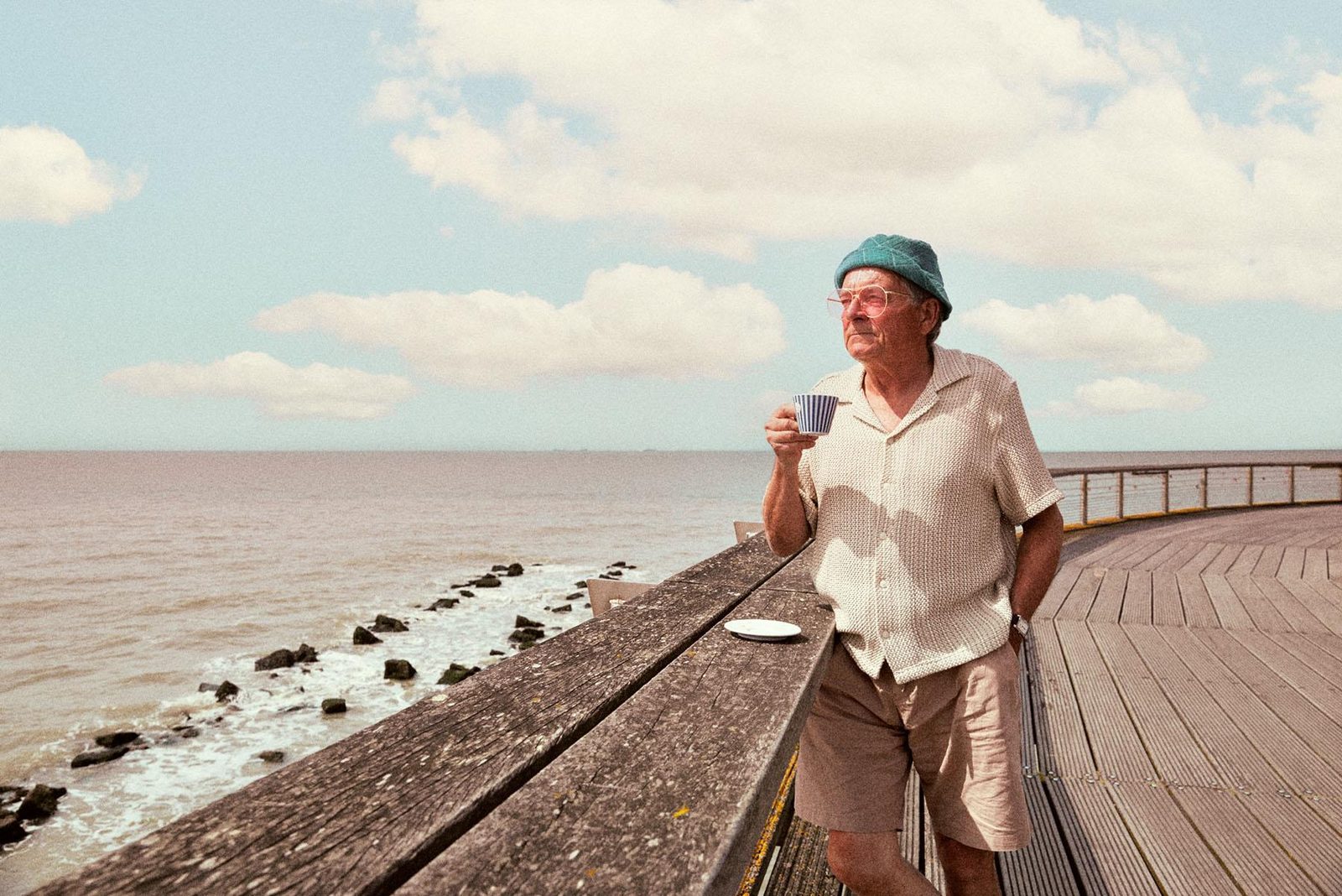 Een oudere man geniet van het uitzicht op zee met een koffie